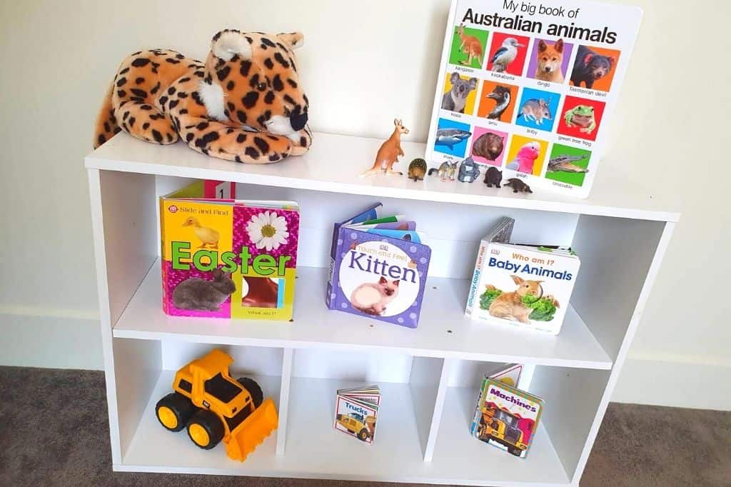Australia Montessori book shelf example with white shelf and 7 books sat upright with a toy loader machine on bottom shelf.