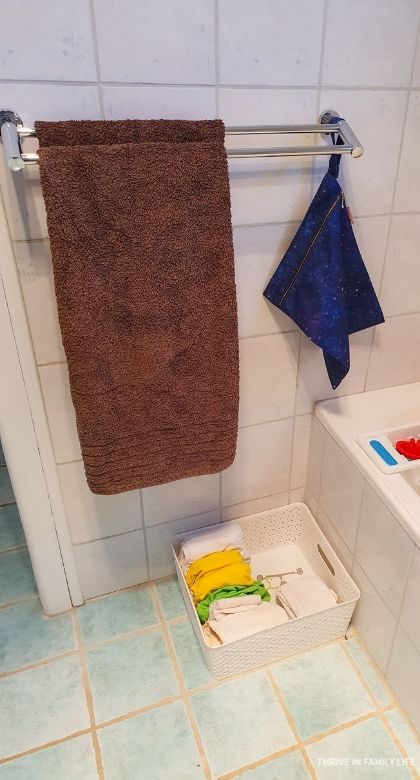 Wet bag on rail in bathroom with white plastic basket with cloth diapers and snappi for standing diaper change