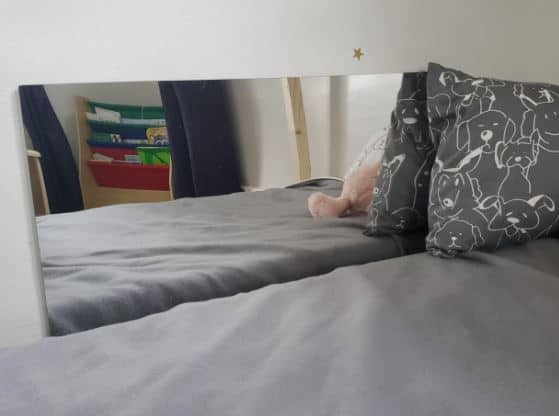 montessori mirror next to a bed with a pillow against wall