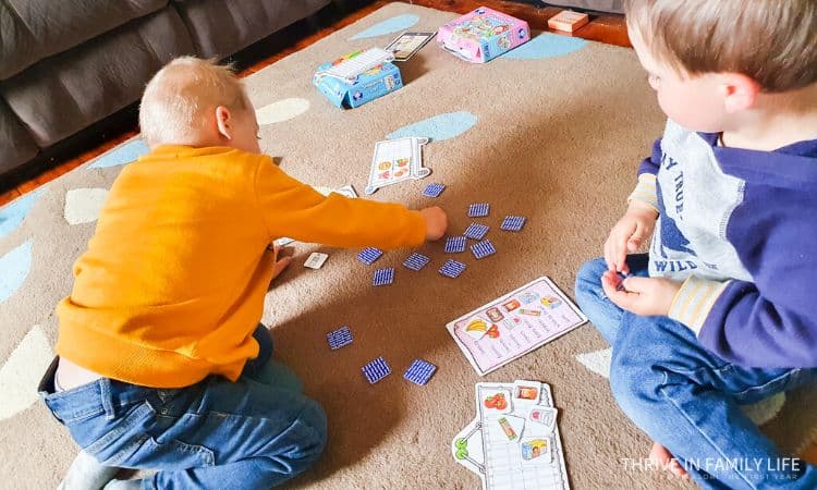 Two toddler boys playing Orchard Toys board game on a beige rug. 