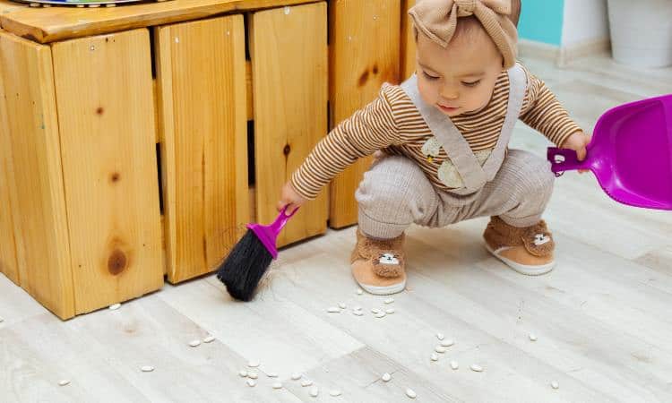 young toddler girl sweeping with purple dust pan and brush