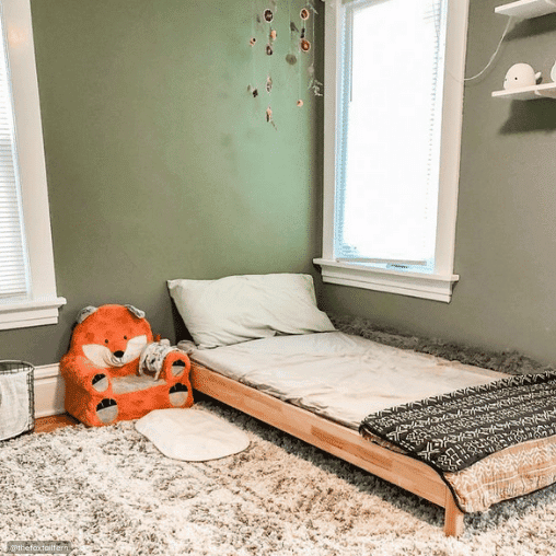 Montessori bed with wooden frame and fox kid chair next to it.