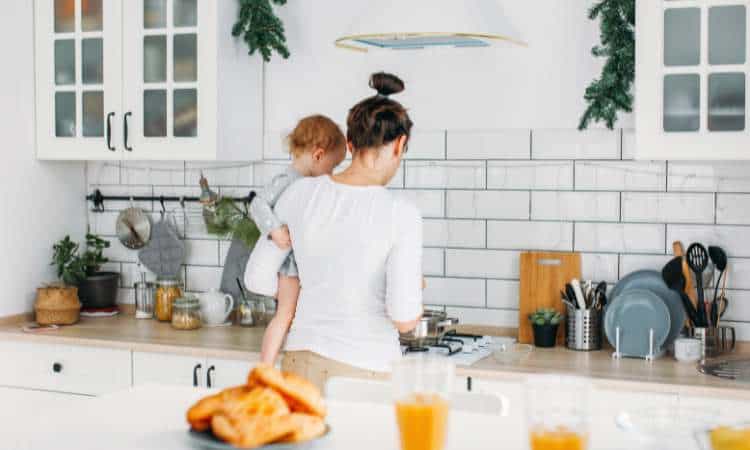 mom holding young toddler on hip while stirring pot on stove