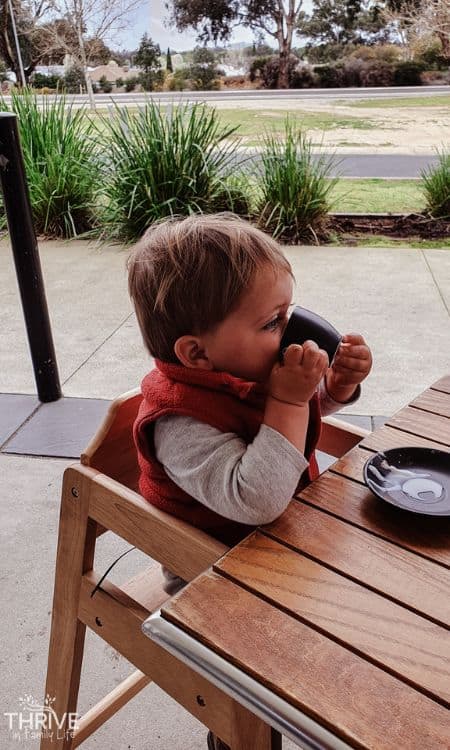 Toddler sitting in high chair drinking a cafe drink from teacup and saucer while at cafe