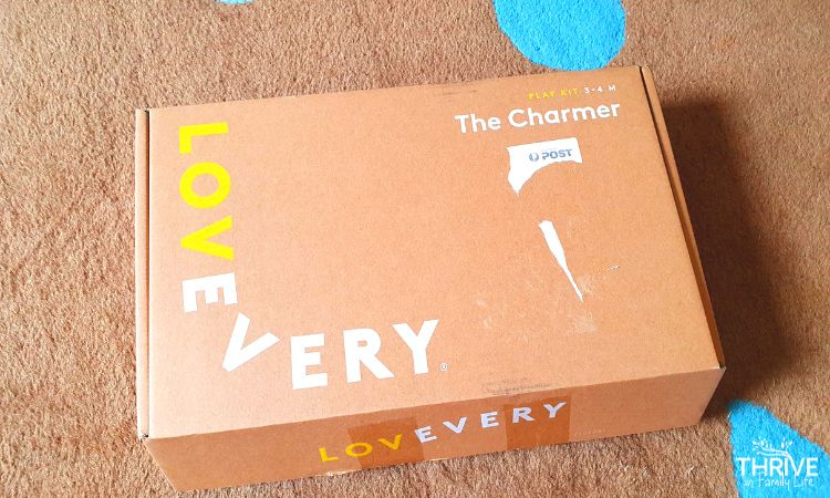 Lovevery Charmer Play Kit box on a brown rug. 